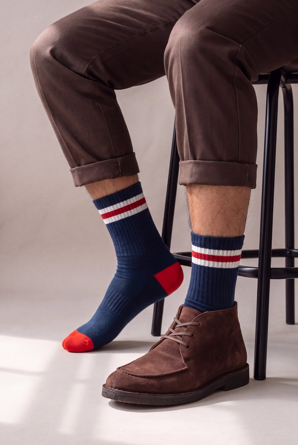 Medias largas azul marino con detalle rojo, en hombre sentado con pantalon cafe y botin de gamuza, cana completa visible