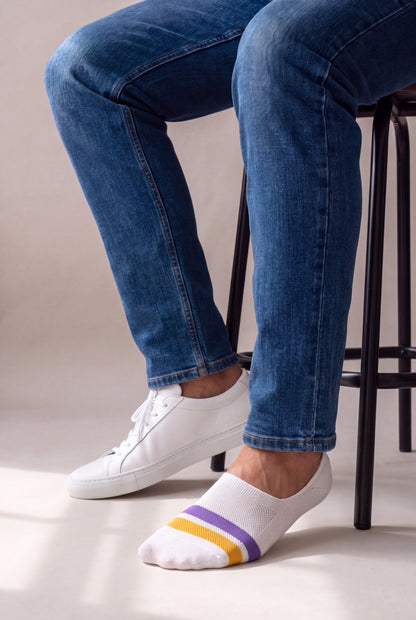 Media tobillera blanca de hombre Luck and Load, corte low-cut invisible con franja amarilla y morada, puesta con tenis blanco.